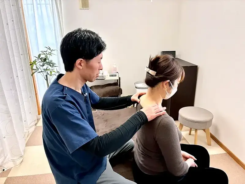 座った姿勢で肩に手を当てて施術している様子