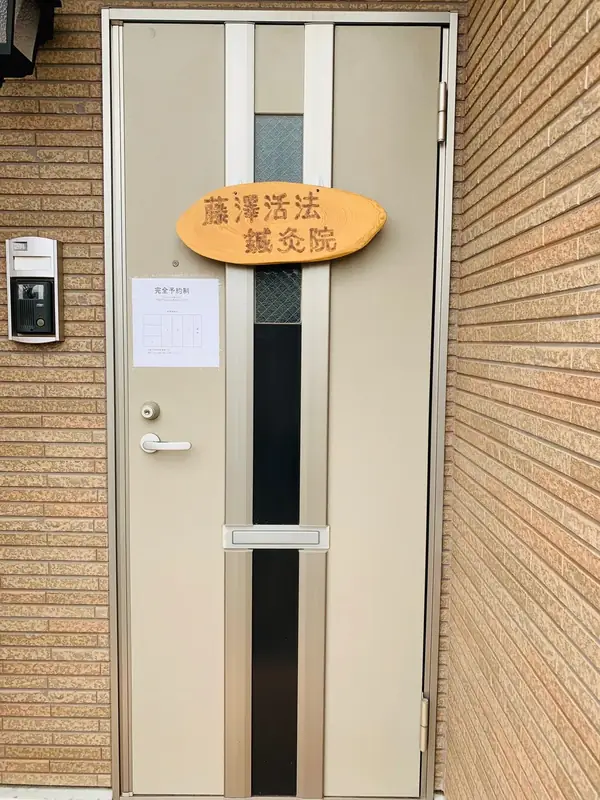 建物の玄関。ドアの上に藤澤活法鍼灸院の木の看板